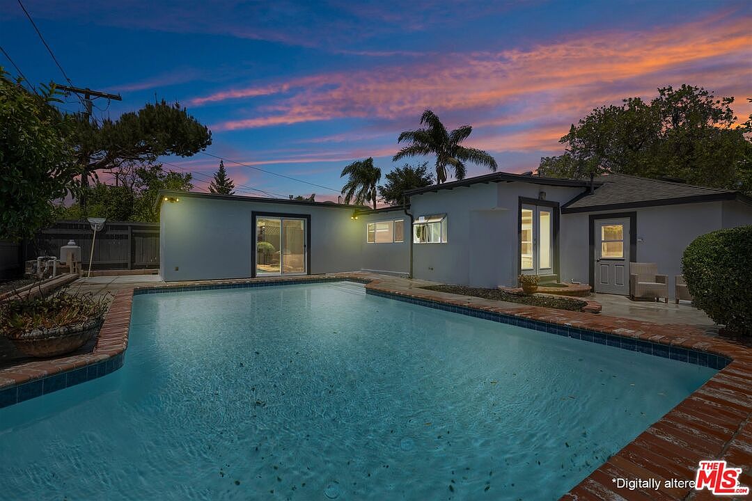 Backyard pool at twilight, the lit water glowing teal under a pink and orange sunset with palm tree silhouettes against the house