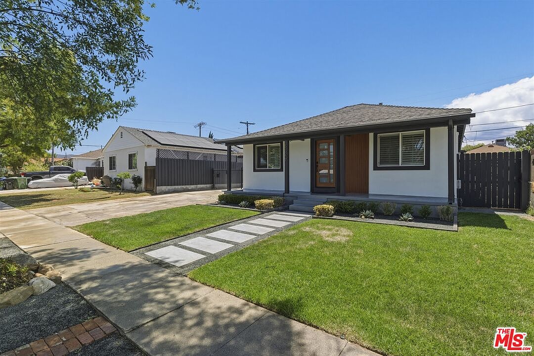 Side three-quarter view of the bungalow showing the porch and pavers from the neighbor's sidewalk angle in midday sun