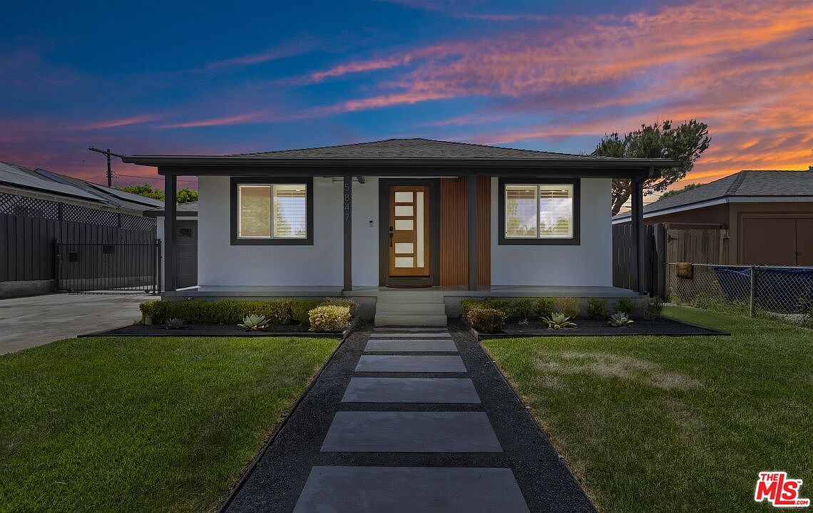 5847 Texhoma Avenue at twilight, the remodeled white bungalow front lit warmly against a pink and orange Valley sunset